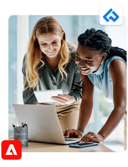 Two women smiling and working together on a laptop and tablet