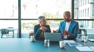 Two coworkers having coffee working on a laptop together