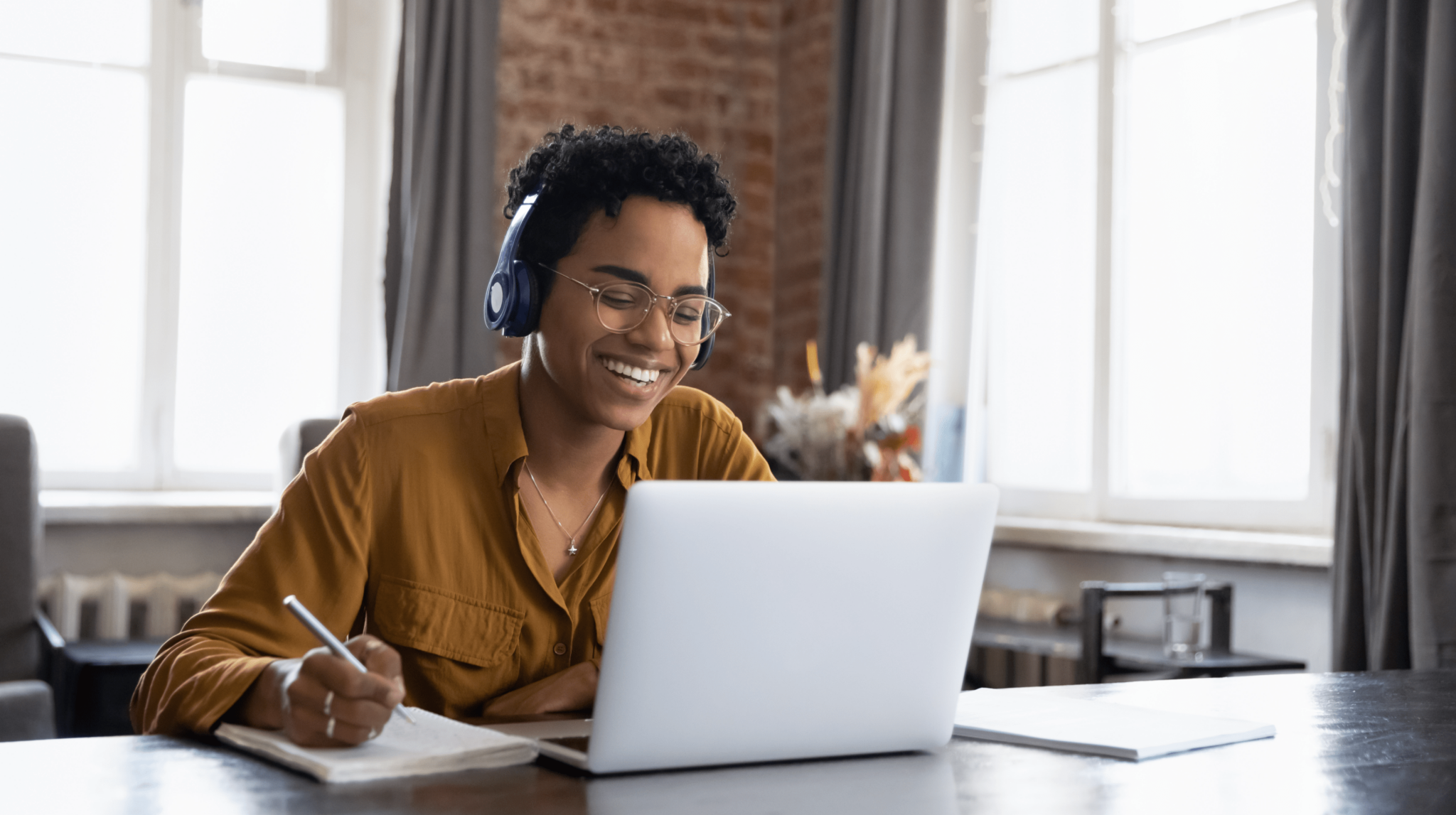 Woman smiling wearing headphones while working on a laptop