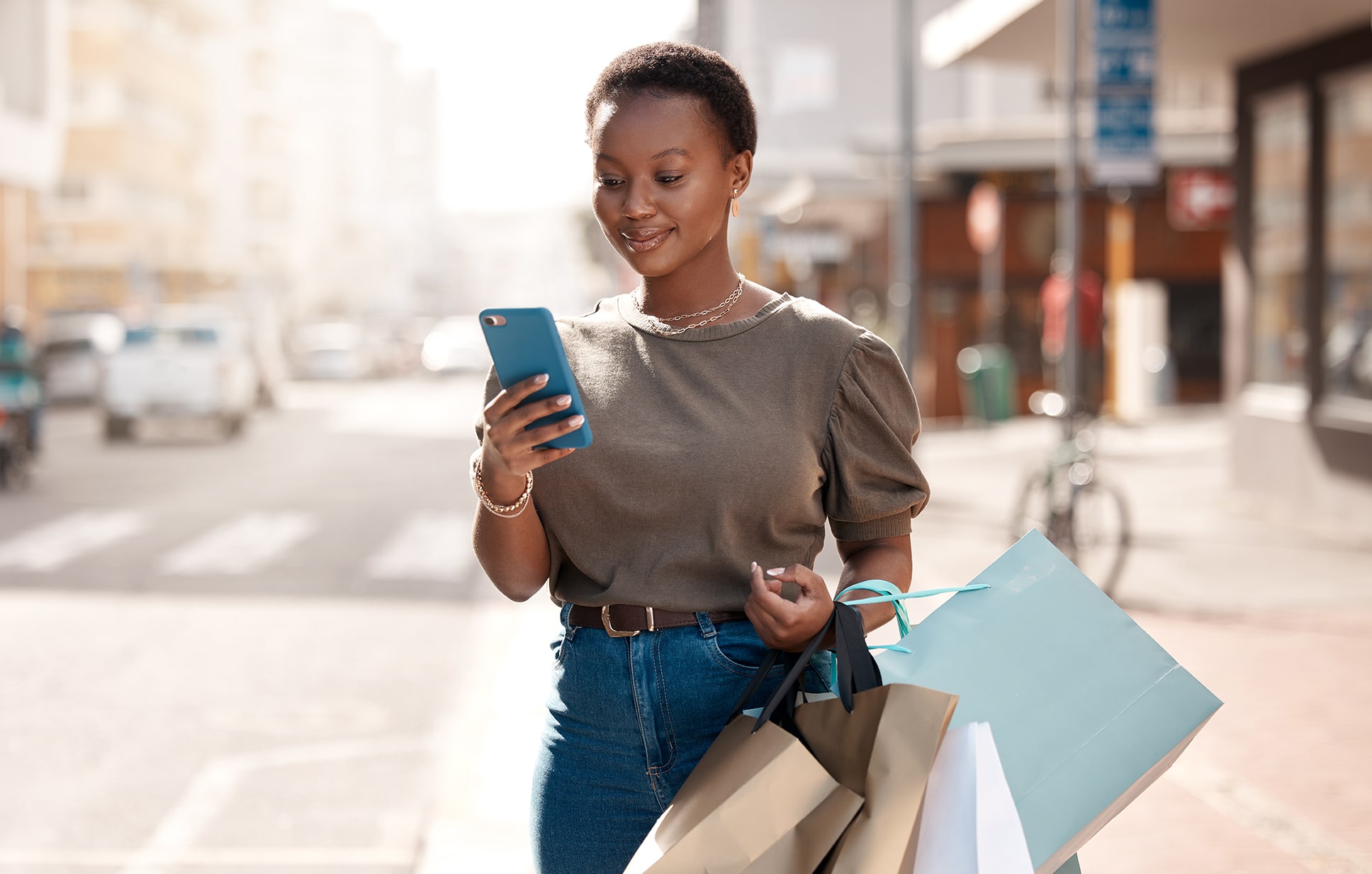 a woman looking at her cell phone, with shopping bags in her hand